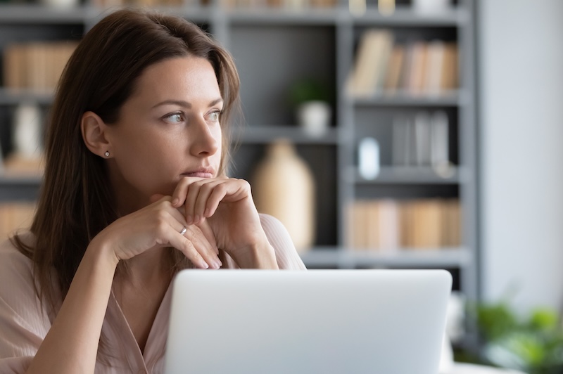 Pensive millennial girl sit at desk look in window distance thinking or dreaming visualizing, thoughtful young woman distracted from computer work pondering over problem solution, lost in thoughts